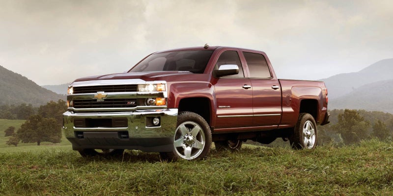 2017 Chevrolet Silverado 2500HD in maroon, parked on a grassy hill with mountains in the background.