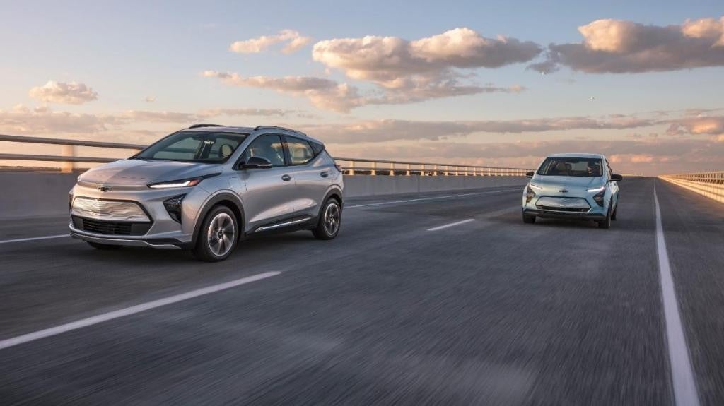 Two Chevrolet Bolt EUVs driving on a wide bridge highway at sunset, showcasing the car's modern electric design.
