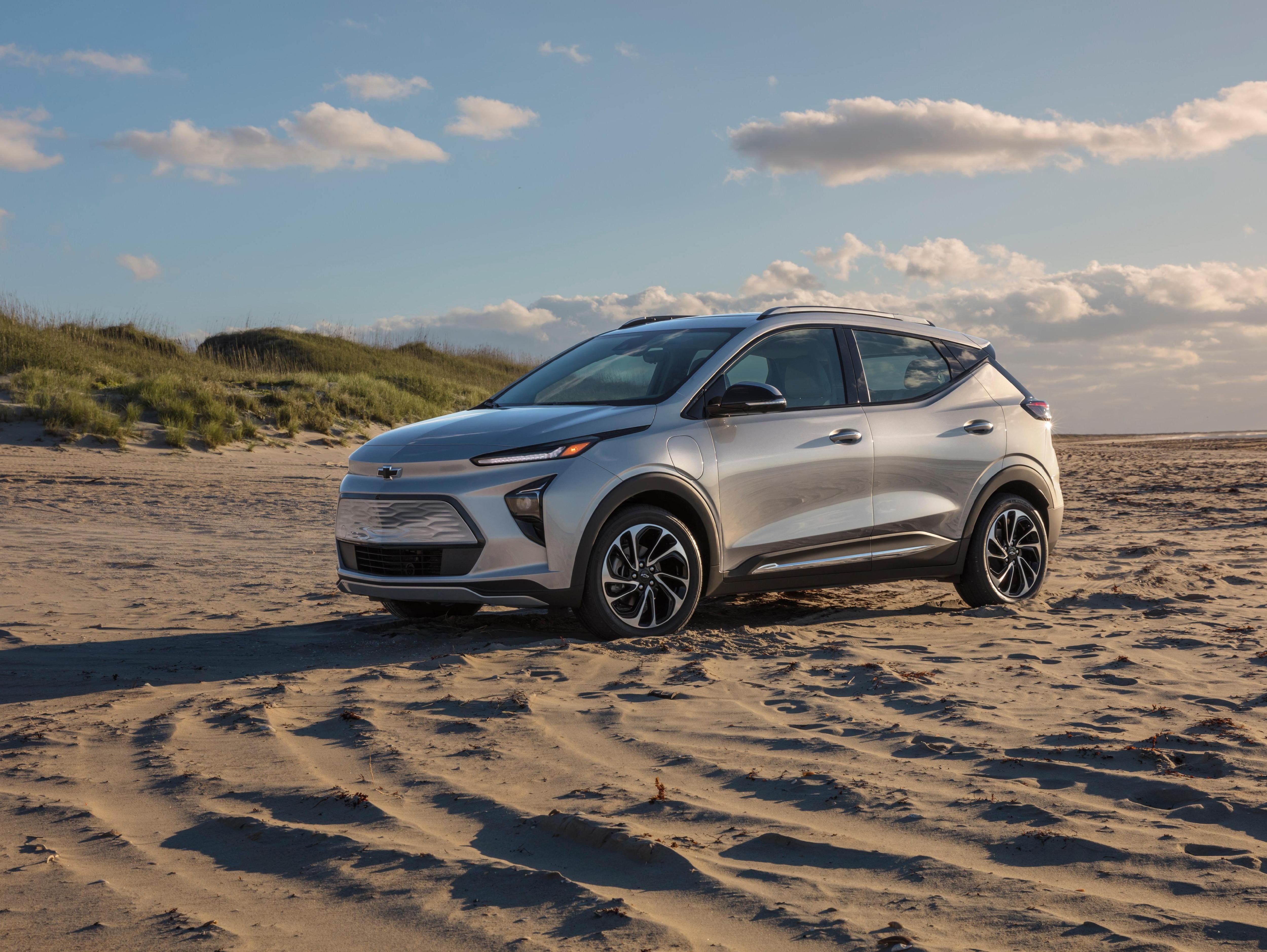 Chevrolet Bolt EUV parked on a sandy beach with grassy dunes in the background under a partly cloudy sky.